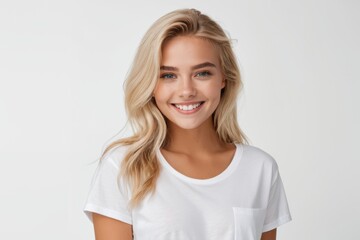 Fototapeta premium The image shows a woman with long blonde hair wearing a white t-shirt, smiling brightly against a white background.