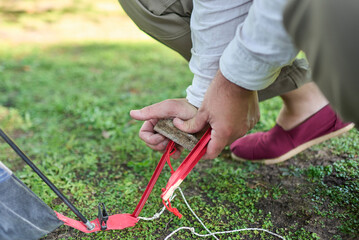 Unknown person using a stone as a hammer to drive a tent peg into the ground.