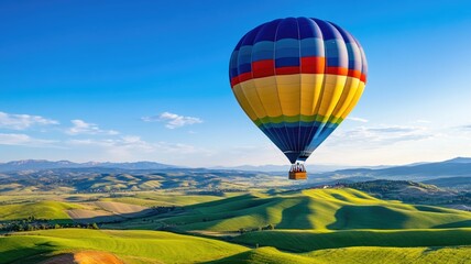Fototapeta premium Colorful hot air balloon floating over lush green hills on clear day