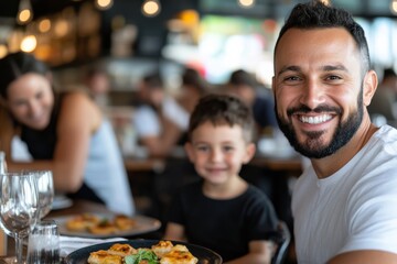 A joyful father smiles for the camera while his young son playfully poses beside him at a cozy restaurant table with delicious pizza in front, creating a warm dining experience.