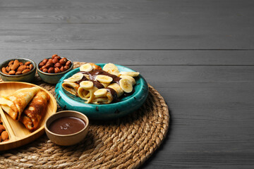 Delicious crepes served with chocolate paste and nuts on grey wooden table, space for text