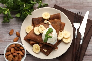 Delicious chocolate crepes with banana, nuts, mint and scoop of ice cream on wooden table, flat lay