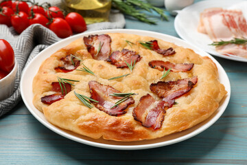 Delicious focaccia bread with bacon, rosemary and tomatoes on light blue wooden table, closeup