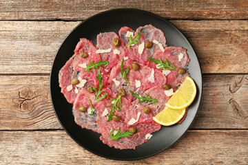 Delicious beef carpaccio with arugula, capers, cheese and lemon on wooden table, top view
