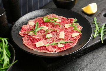 Fresh beef carpaccio with arugula and cheese on dark textured table, closeup