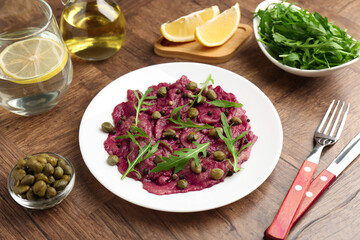 Fresh beef carpaccio with arugula and capers on wooden table