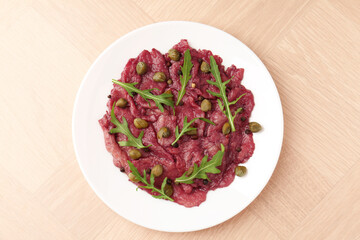 Fresh beef carpaccio with arugula and capers on wooden table, top view