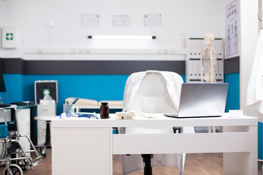 Organized, empty hospital room with desk, chair, and healthcare technology for efficient patient care. Modern, clean doctors office having a laptop and medical equipment on white table.