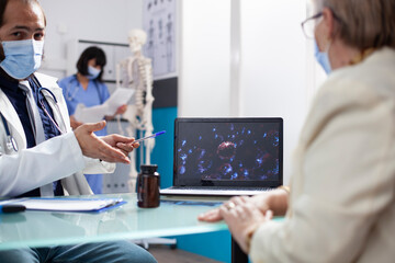 Doctor consults with old woman in clinic showing enlarged flu virus illustration during diagnosis...