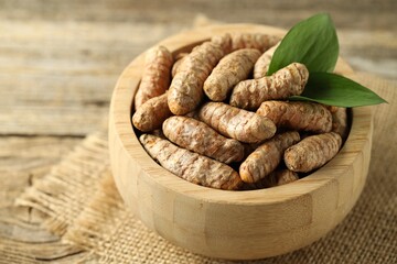 Tumeric rhizomes with leaves in bowl on wooden table, closeup