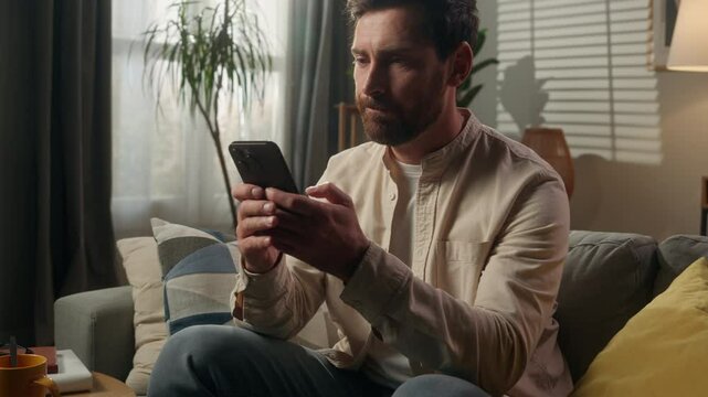Male homeowner angry man Caucasian businessman guy browsing mobile phone at home apartment frustrated confused bad message upset trouble problem smartphone texting sms online social media internet app