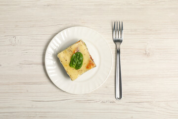 Piece of delicious spinach lasagne and fork on white wooden table, top view