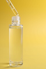 Dripping serum from pipette into bottle on yellow background, closeup. Space for text