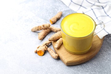 Tasty turmeric latte in cup and roots on grey table, closeup. Space for text