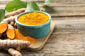 Turmeric powder in bowl, roots and leaves on wooden table, closeup. Space for text