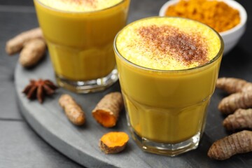 Delicious turmeric latte, powder and rhizomes on black wooden table, closeup