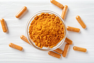 Turmeric capsules and powder on white wooden table, flat lay