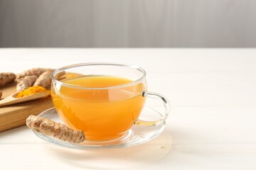 Aromatic turmeric tea in glass cup, roots and powder on white wooden table, closeup. Space for text
