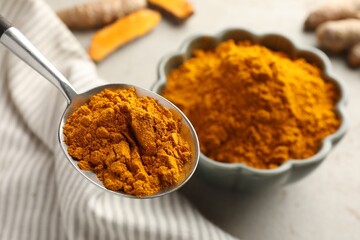 Turmeric powder in spoon at light grey table, closeup
