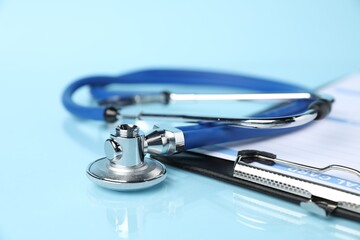 Stethoscope and medical card form on light blue background, closeup
