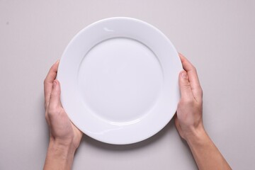 Man with clean plate at light grey table, top view