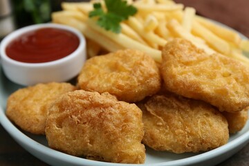 Tasty chicken nuggets and french fries with sauce on wooden table, closeup