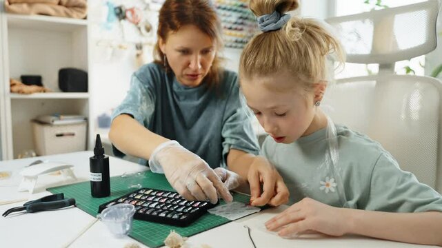 Close-up of hands creating custom jewelry with resin. Child and parent work together, pouring vibrant resin into tiny molds. Handmade art project helps develop creativity, patience, fine motor skills.