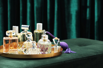 Different luxury perfumes on green pouf near teal curtains, space for text