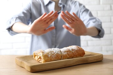 Woman refusing to eat apple strudel at wooden table near white brick wall, selective focus. Food...