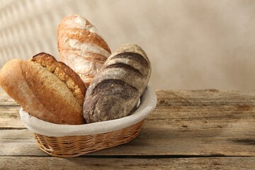 Different loaves of fresh bread in basket on wooden table, closeup. Space for text