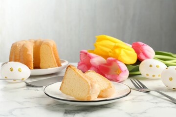 Pieces of delicious bundt cake, Easter eggs and tulips on light marble table