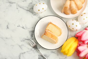 Delicious bundt cake, Easter eggs and tulips on light marble table, flat lay. Space for text