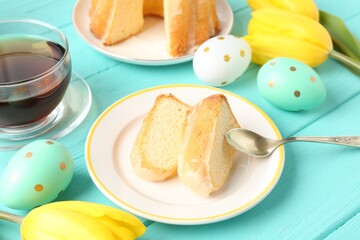 Pieces of delicious bundt cake, Easter eggs, tulips and tea on light blue wooden table, closeup