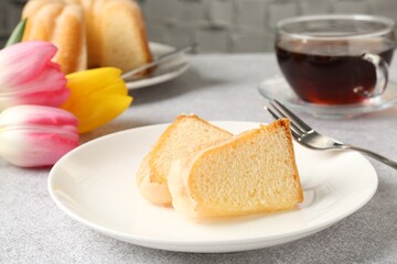 Pieces of delicious bundt cake, tulips and tea on gray table, closeup