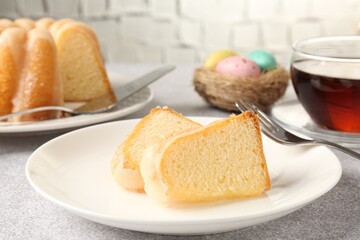 Pieces of delicious bundt cake, Easter eggs and tea on gray table, closeup
