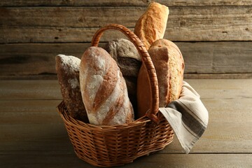 Different loaves of fresh bread in wicker basket on wooden table
