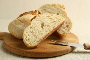 Slices of fresh bread and knife on light textured table, closeup