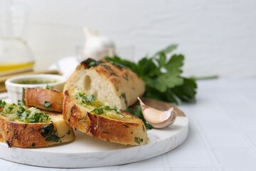 Tasty bread with garlic, herbs and oil on white tiled table, closeup. Space for text