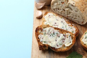 Tasty bread with garlic, herbs and butter on light blue background, closeup. Space for text