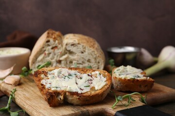 Tasty bread with garlic, herbs and oil on wooden table, closeup
