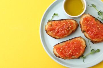 Tasty bread with tomato, microgreens and oil on yellow background, top view. Space for text