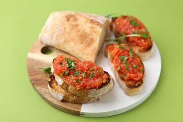 Tasty bread with tomato and parsley on green background, closeup