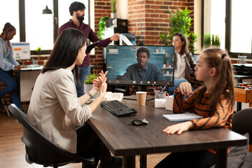In marketing agency office, working mother sharing office desk with little girl and having virtual...