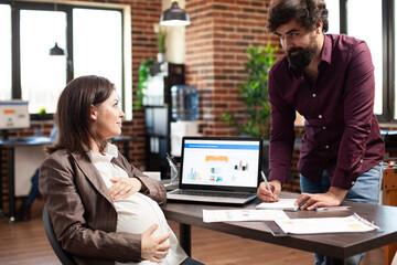 Businessman writing on notebook and doing company research with pregnant colleague at startup...