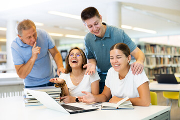 Fototapeta premium Mature man placing fingers on lips with shh near a table with laughing women using computer in the library