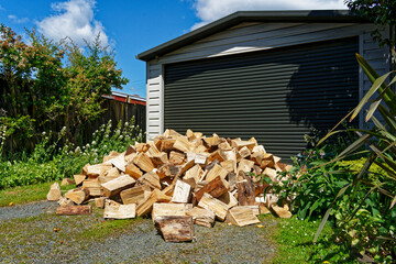 A pile of split firewood logs on a driveway in front of a garage, New Zealand.