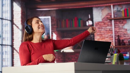 Female freelancer using ambience music on headphones to solve her tasks efficiently, working at...