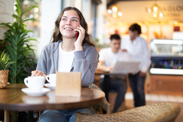 Young woman talking on mobile phone and drinking coffee in cafe