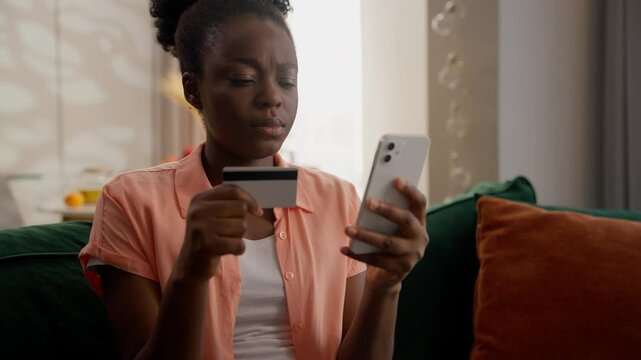 Confused upset African American ethnic business woman female girl businesswoman homeowner holding credit card using mobile phone fail online pay bank app error no money scam fraud transaction at home