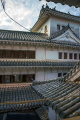 Fototapeta premium Himeji, Japan - Sep 24 2024, vertical, panoramic view from window of roofs and towers with roof tiles in courtyard of Himeji Castle, White Heron Castle, at daytime with cloudy sky, Himeji, Japan